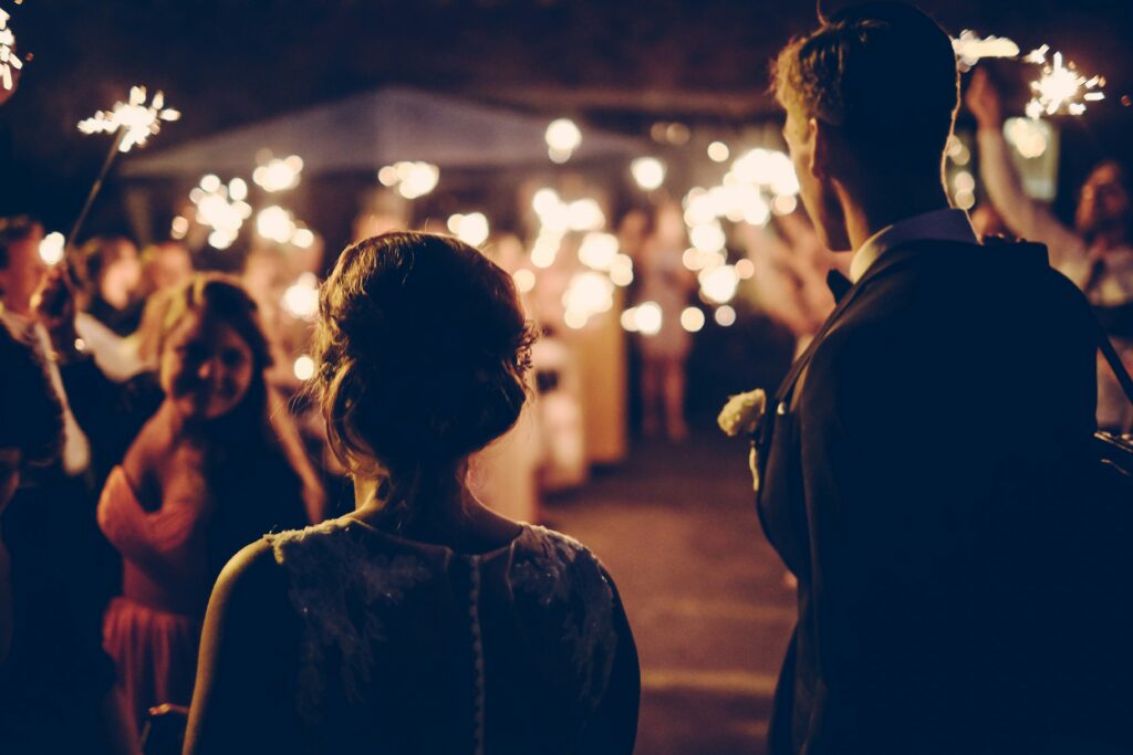 A bride and groom at their wedding ceremony, outside, with guests holding sparklers