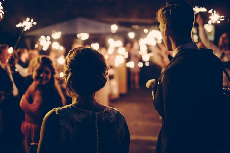 A bride and groom at their wedding ceremony, outside, with guests holding sparklers