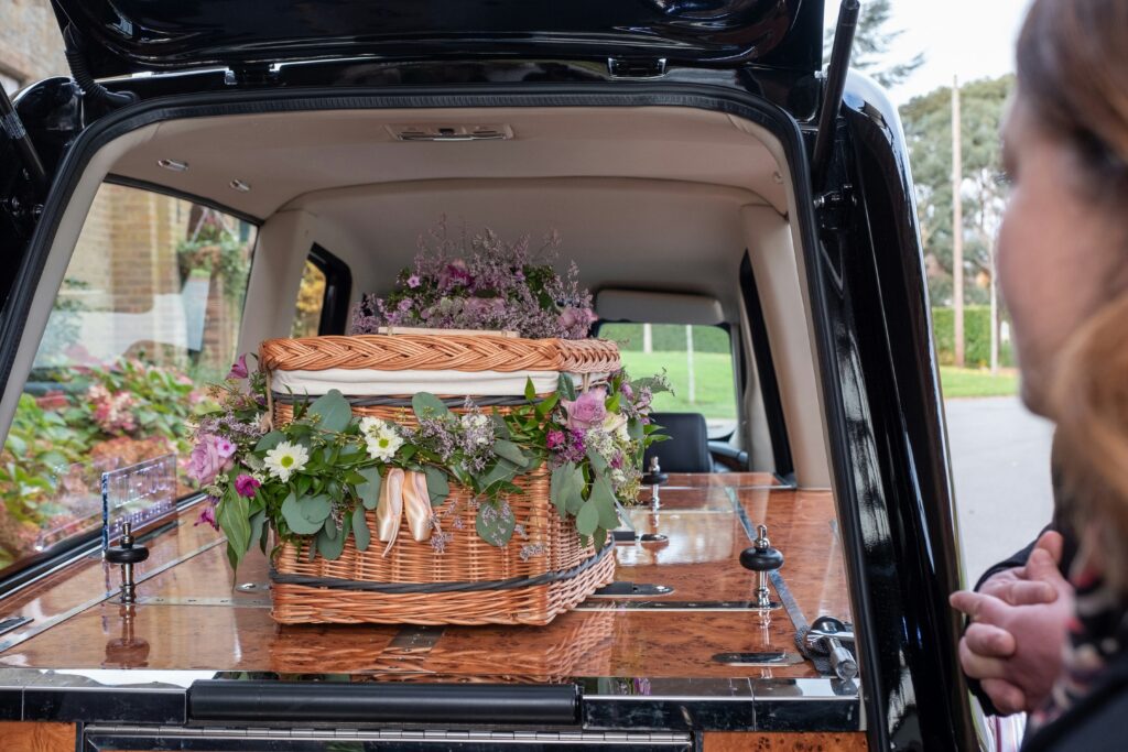 A willow coffin decorated with flowers in the back of a hearse